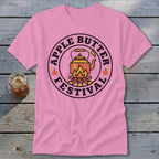 Pink t-shirt with circular graphic featuring a kettle over a campfire and text "Apple Butter Festival".