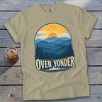 A tan t-shirt with a vintage graphic of mountains, pine trees, and the text OVER YONDER.