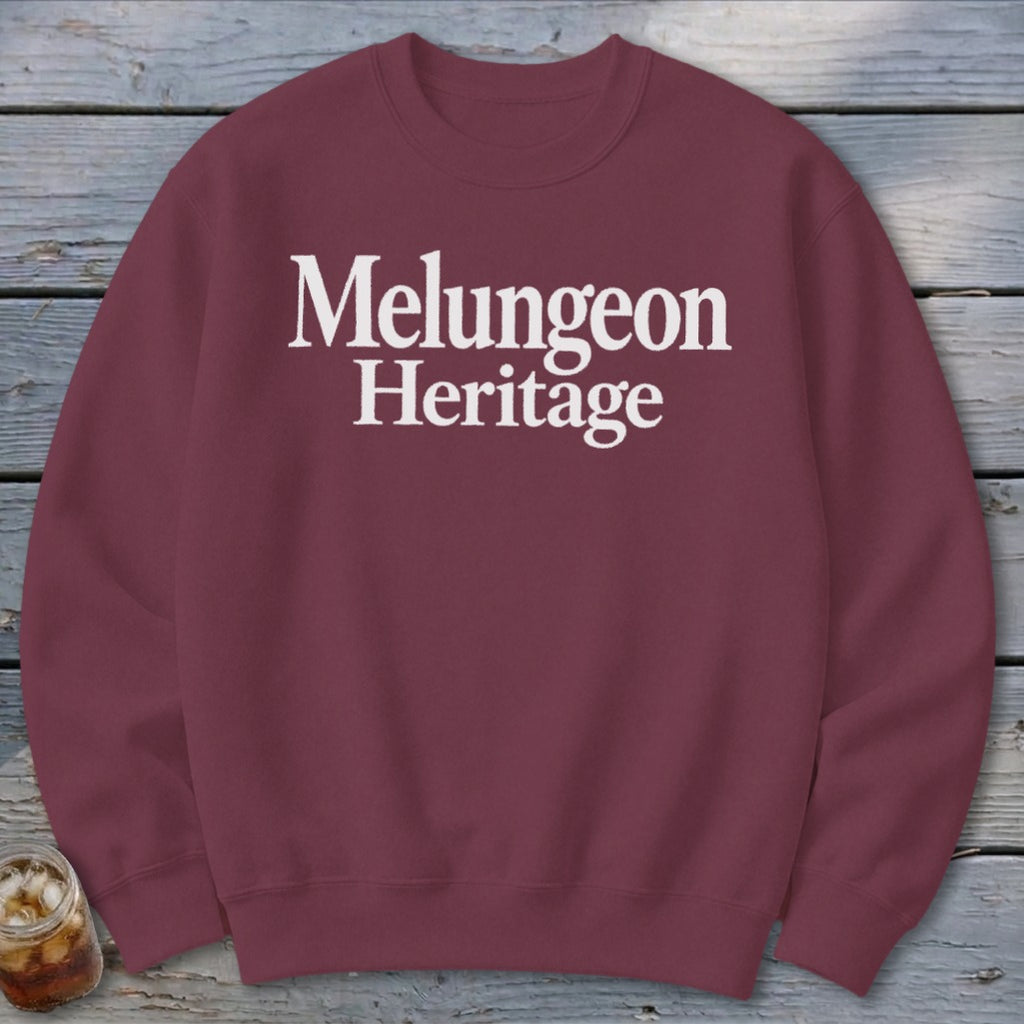Maroon crewneck sweatshirt featuring white text that reads Melungeon Heritage, displayed on a wooden background.