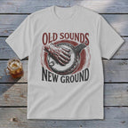A light gray t-shirt with a vintage graphic of a hand playing a banjo and text reading Old Sounds New Ground.