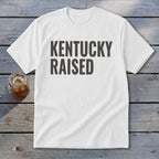 White t-shirt with dark gray text that reads "KENTUCKY RAISED".