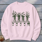 A light pink crewneck sweatshirt featuring a dark green graphic of four mason jars filled with wildflowers on a wooden shelf.