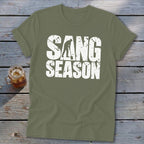 An olive green t-shirt with distressed white text reading SANG SEASON and a silhouette digging.