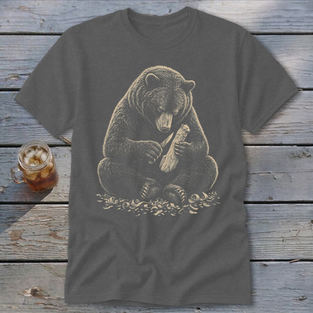 Bear sitting, carving wood with a knife, on a dark grey t-shirt.