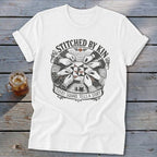 White t-shirt with graphic of hands quilting with text "Stitched By Kin" and "Every Square Tells A Story".