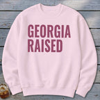 Light pink sweatshirt with "GEORGIA RAISED" printed in dark pink.