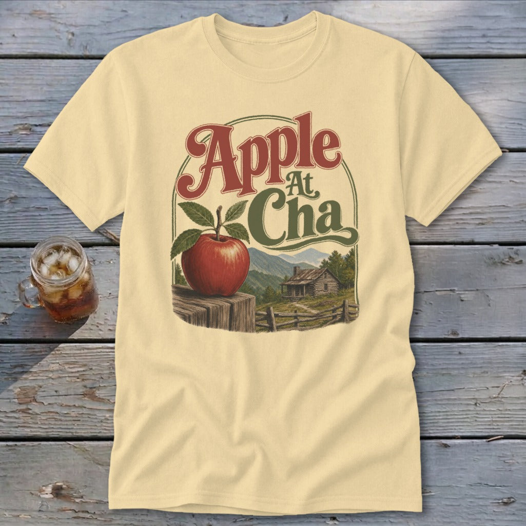 Cream t-shirt featuring a graphic with an apple, cabin scenery, and the text Apple At Cha.
