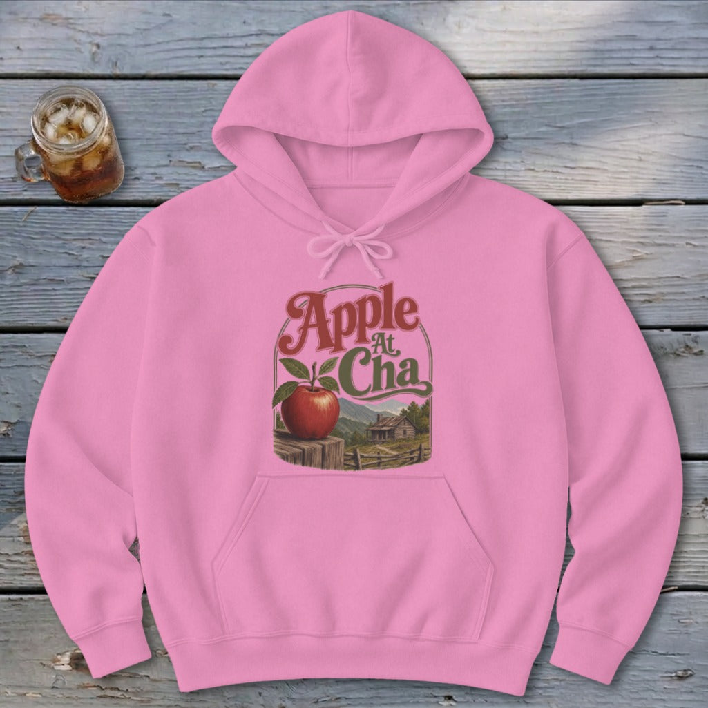 A pink pullover hoodie featuring a graphic of an apple, a cabin, and text reading Apple At Cha.