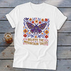 White t-shirt with a purple moth design and the text "Believe the Mountain Tales".