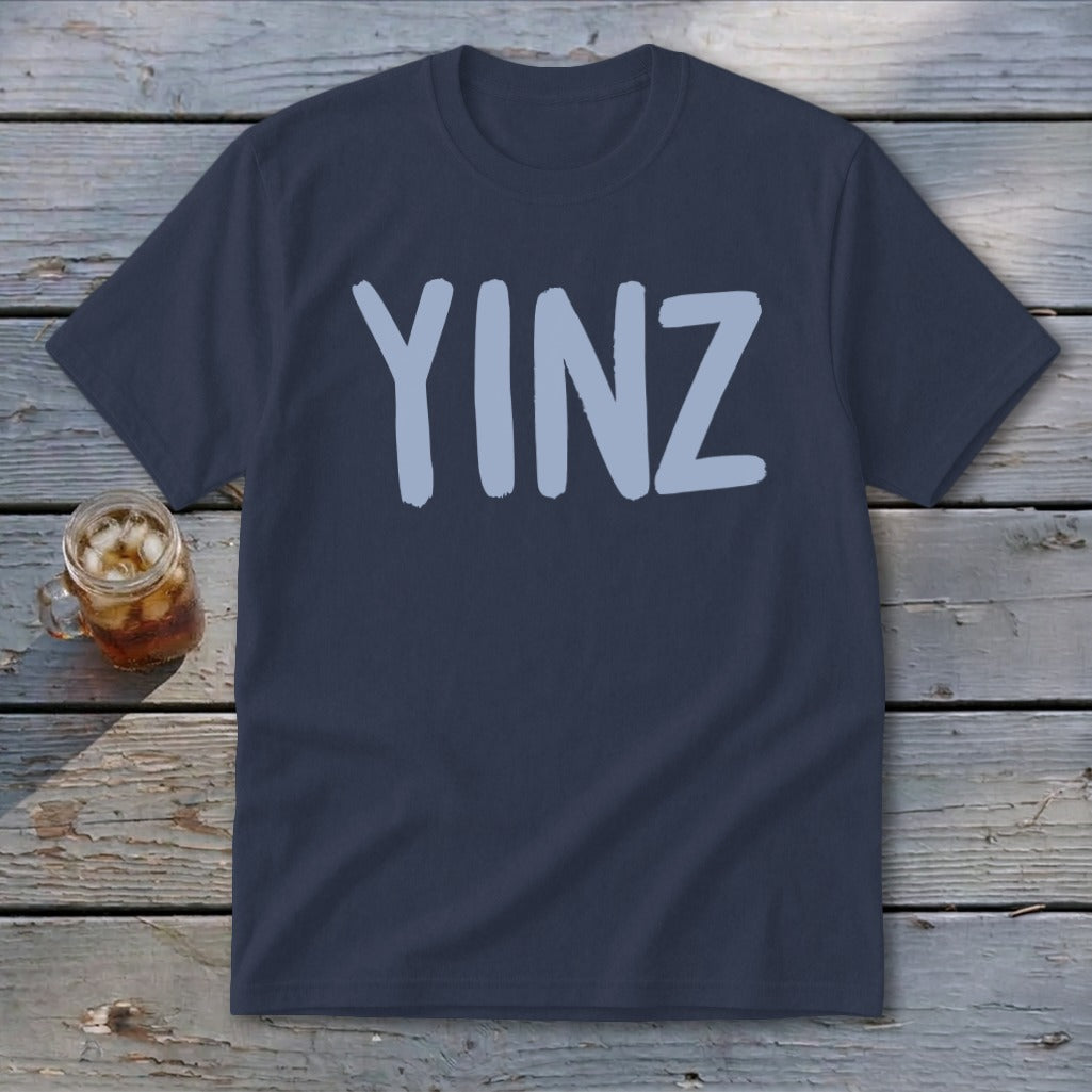 Dark blue t-shirt with light blue "YINZ" text, beside a glass of iced beverage.