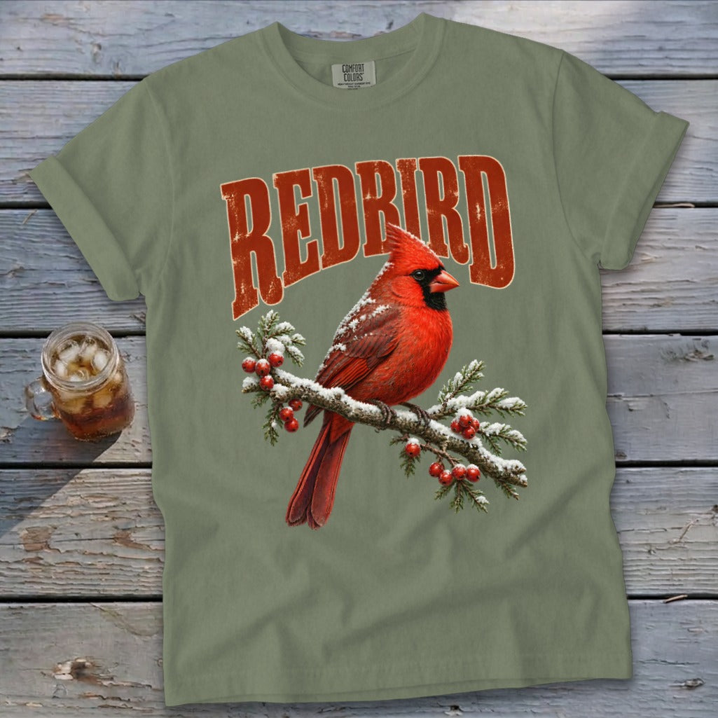 Olive green t-shirt featuring a graphic of a red cardinal on a snowy branch with red text above it.