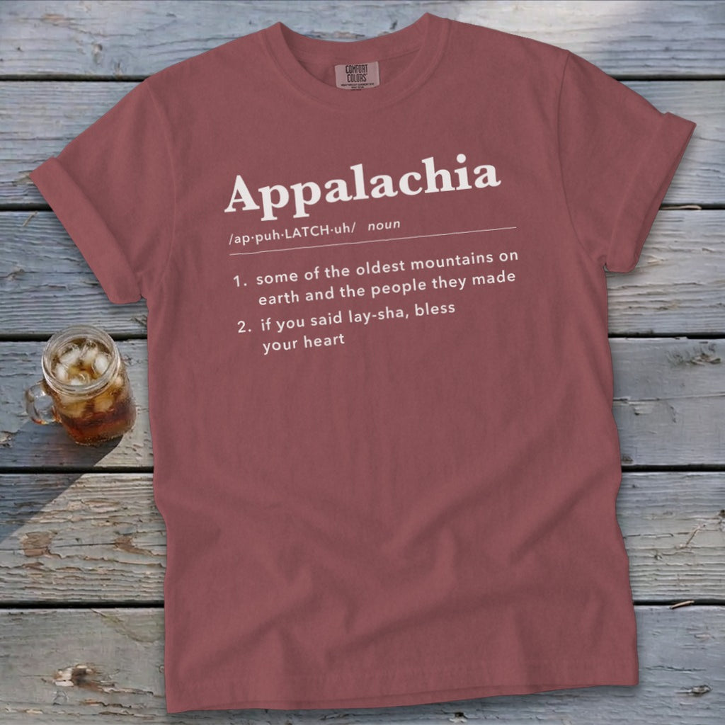 A mauve t-shirt laying on a wooden surface displays white text defining Appalachia.