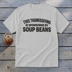 A light grey t-shirt featuring black text that reads THIS THANKSGIVING IS SPONSORED BY SOUP BEANS.