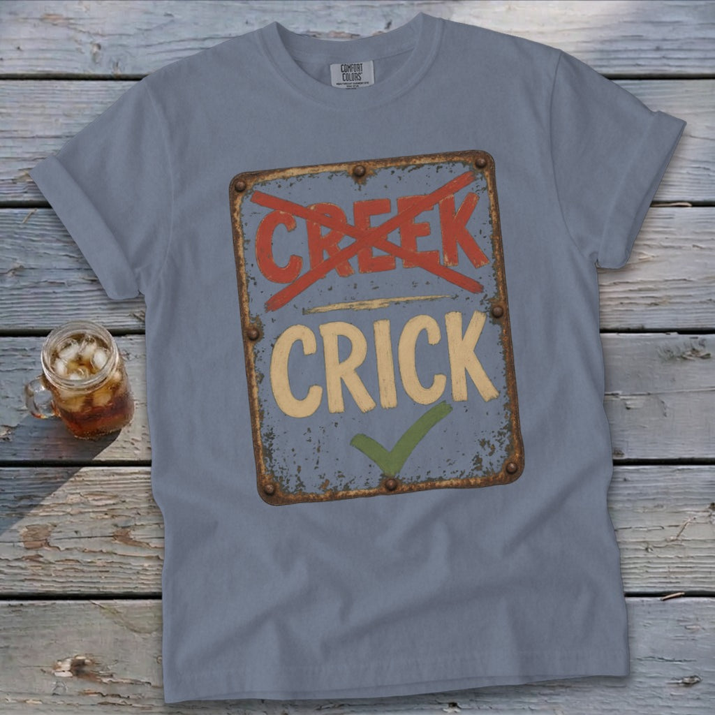 Blue t-shirt with a distressed sign graphic reading "CREEK" crossed out and "CRICK" with a checkmark.