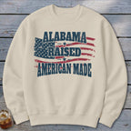 Cream sweatshirt with distressed "Alabama Raised American Made" text over a US flag design.