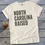 Cream t-shirt with "North Carolina Raised" text in dark gray lettering.