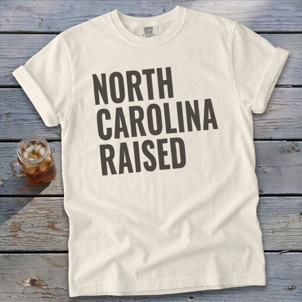 Cream t-shirt with "North Carolina Raised" text in dark gray lettering.