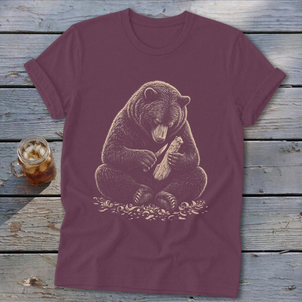 Bear carving wood with a knife on a burgundy t-shirt.
