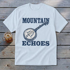 A light blue t-shirt with a blue graphic of a banjo and the text Mountain Echoes.