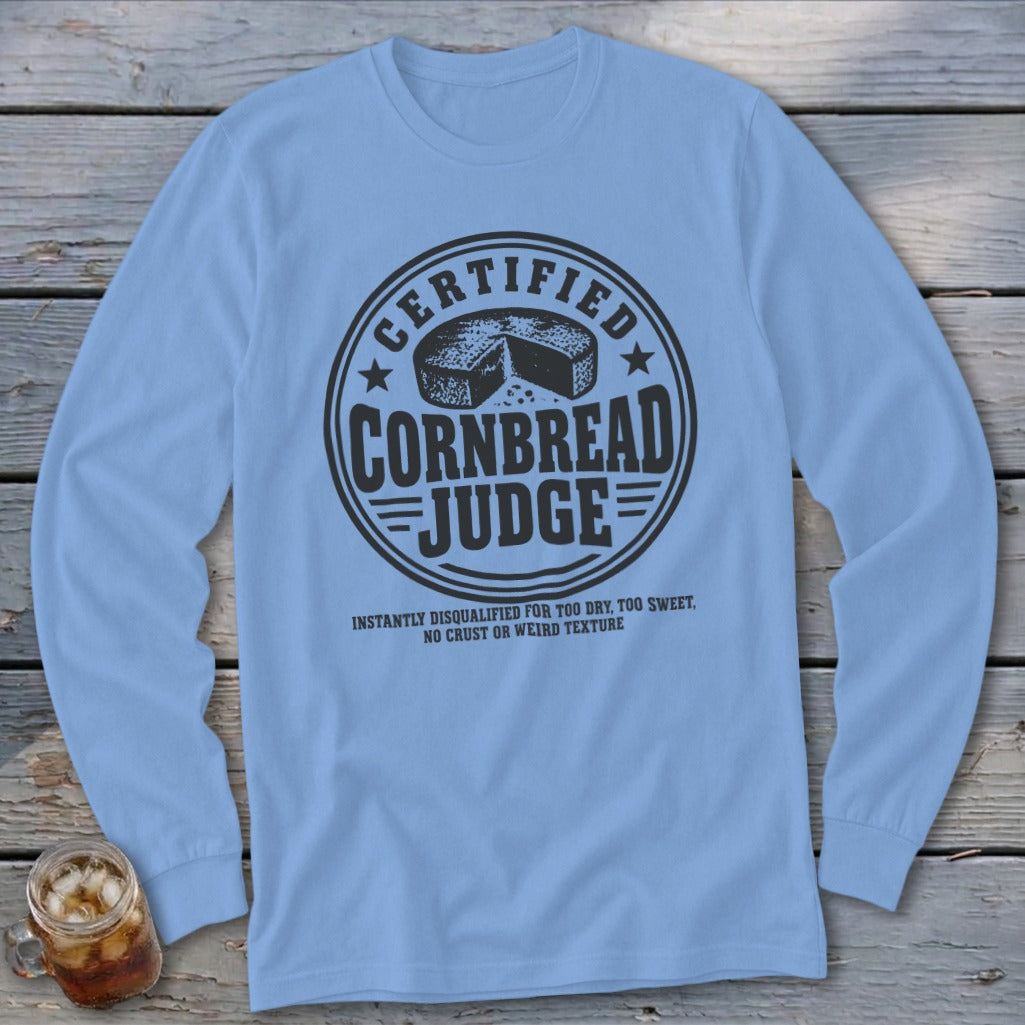 A light blue long-sleeve t-shirt with a round black graphic featuring a cornbread wheel and text.