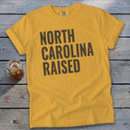 Yellow t-shirt with "NORTH CAROLINA RAISED" text in dark gray.