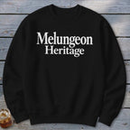 Black crewneck sweatshirt featuring white text that reads Melungeon Heritage centered on the chest, laid flat against a weathered wooden background.