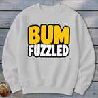 A light gray crewneck sweatshirt displays the text BUM FUZZLED in bold, uppercase cartoon letters centered on the chest.