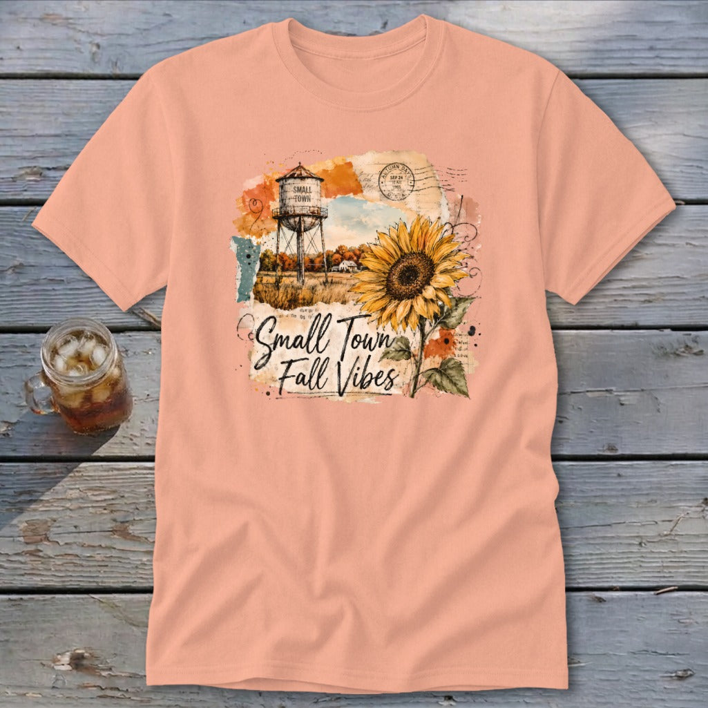 Peach t-shirt with a graphic of a water tower, sunflower, and text reading "Small Town Fall Vibes."