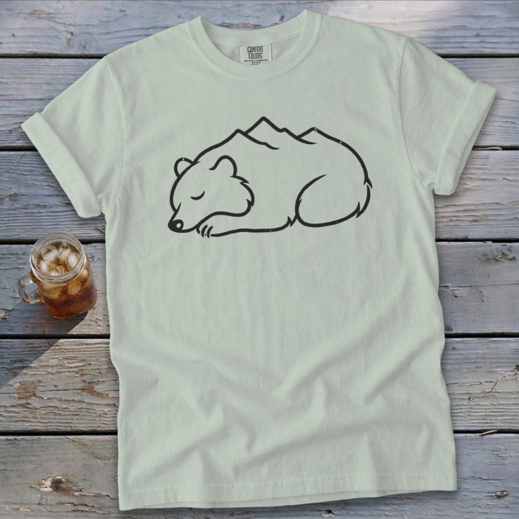 Light green t-shirt with a black line drawing of a sleeping bear integrated with mountains.