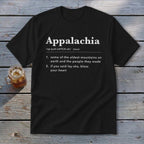 A black t-shirt printed with a dictionary definition of Appalachia rests on a weathered wooden background beside a glass of iced tea.