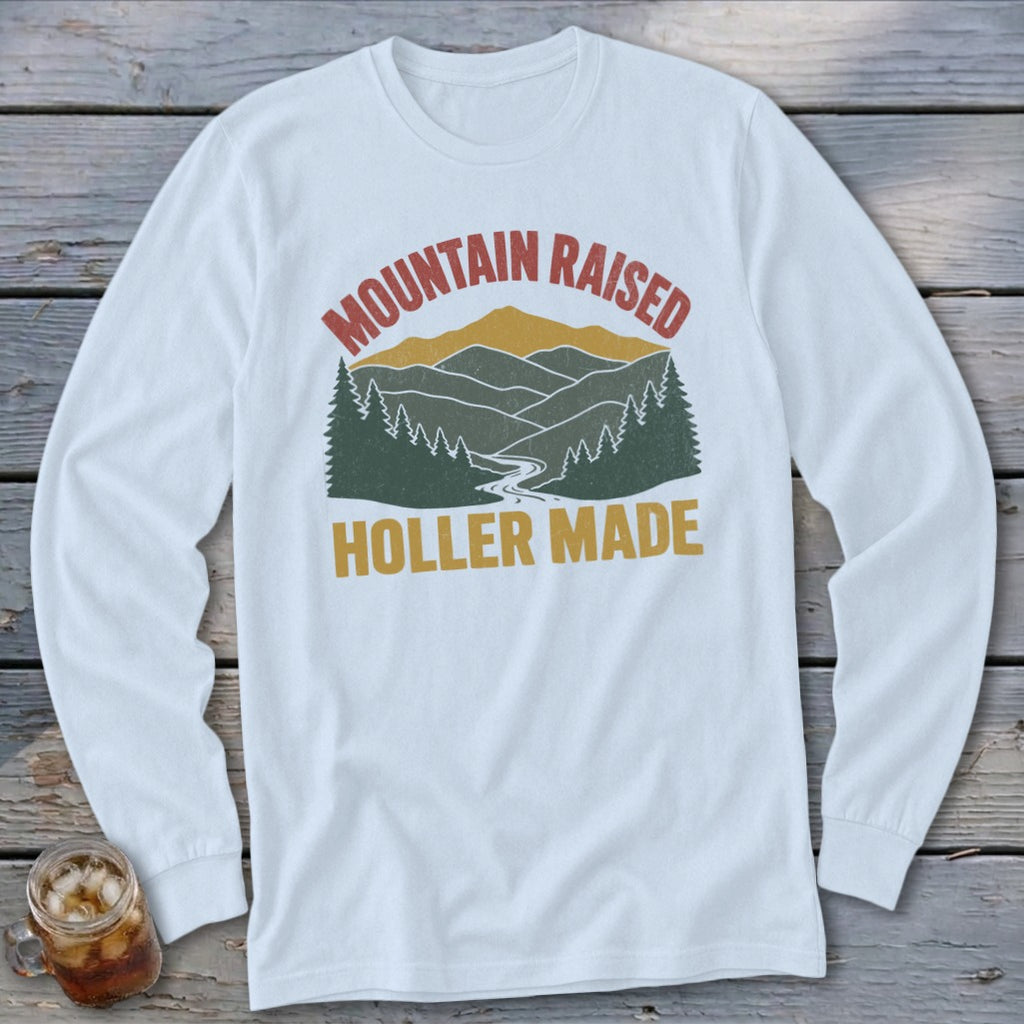 A white long-sleeved t-shirt featuring a retro mountain landscape graphic with the text Mountain Raised and Holler Made.