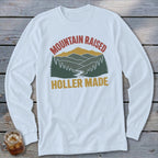 A white long-sleeved t-shirt featuring a retro mountain landscape graphic with the text Mountain Raised and Holler Made.