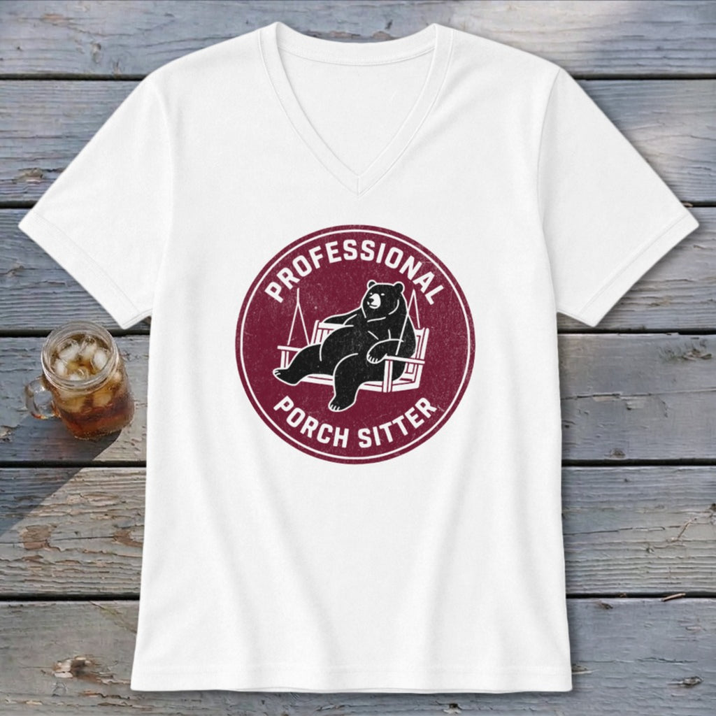 A white V-neck t-shirt featuring a maroon circular graphic of a bear lounging on a porch swing, with the text "PROFESSIONAL PORCH SITTER".