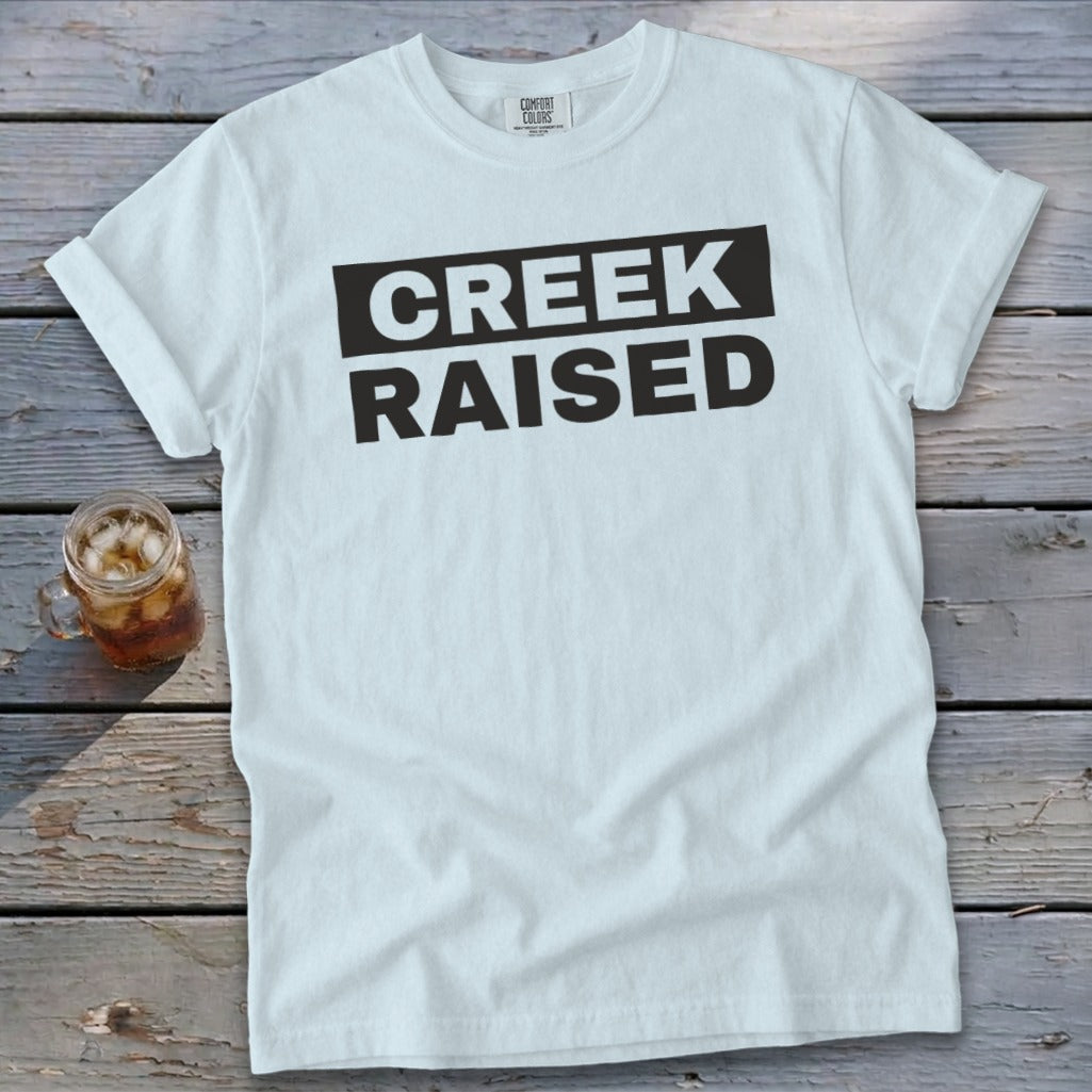 White t-shirt with "CREEK RAISED" printed in black text.
