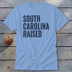 Light blue t-shirt with "SOUTH CAROLINA RAISED" text in dark blue.