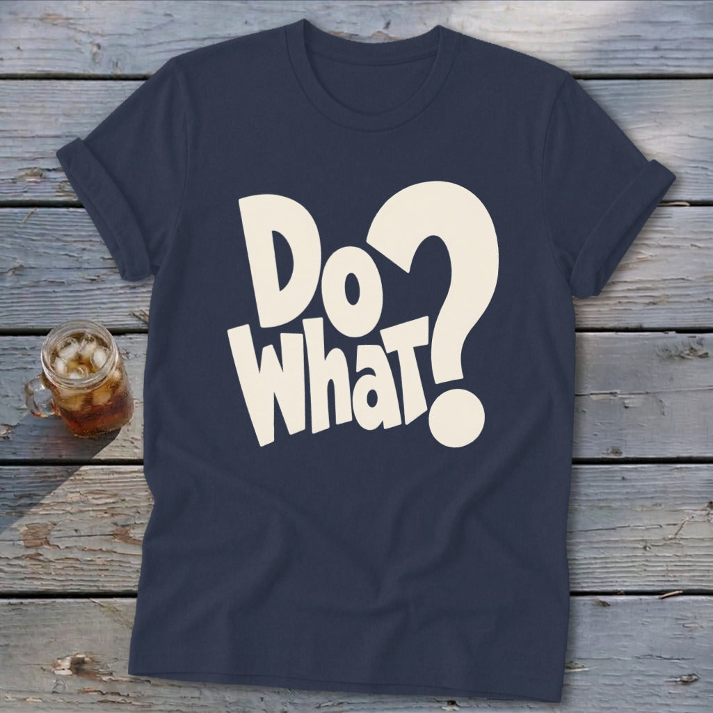 A dark blue t-shirt printed with the white text Do What? rests on a wooden surface beside a glass of iced tea.