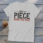 White t-shirt with text "JUST A PIECE DOWN THE ROAD".
