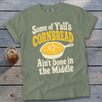 Sage green t-shirt featuring text and a skillet of cornbread laid flat on a rustic wooden background.