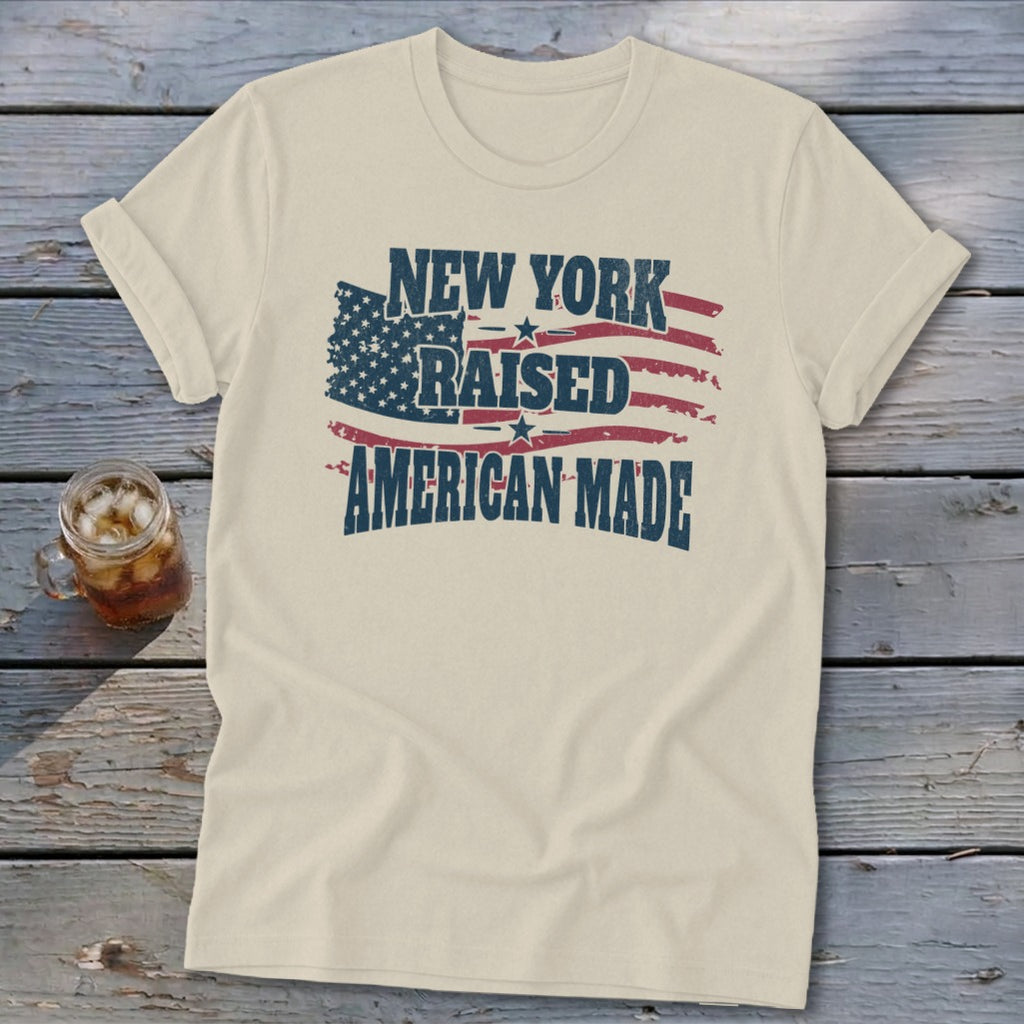 Cream t-shirt featuring distressed text reading "NEW YORK RAISED AMERICAN MADE" over a distressed American flag graphic.