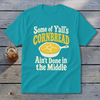 A turquoise t-shirt with the text "Some of Y'all's Cornbread Ain't Done in the Middle" and a skillet graphic.