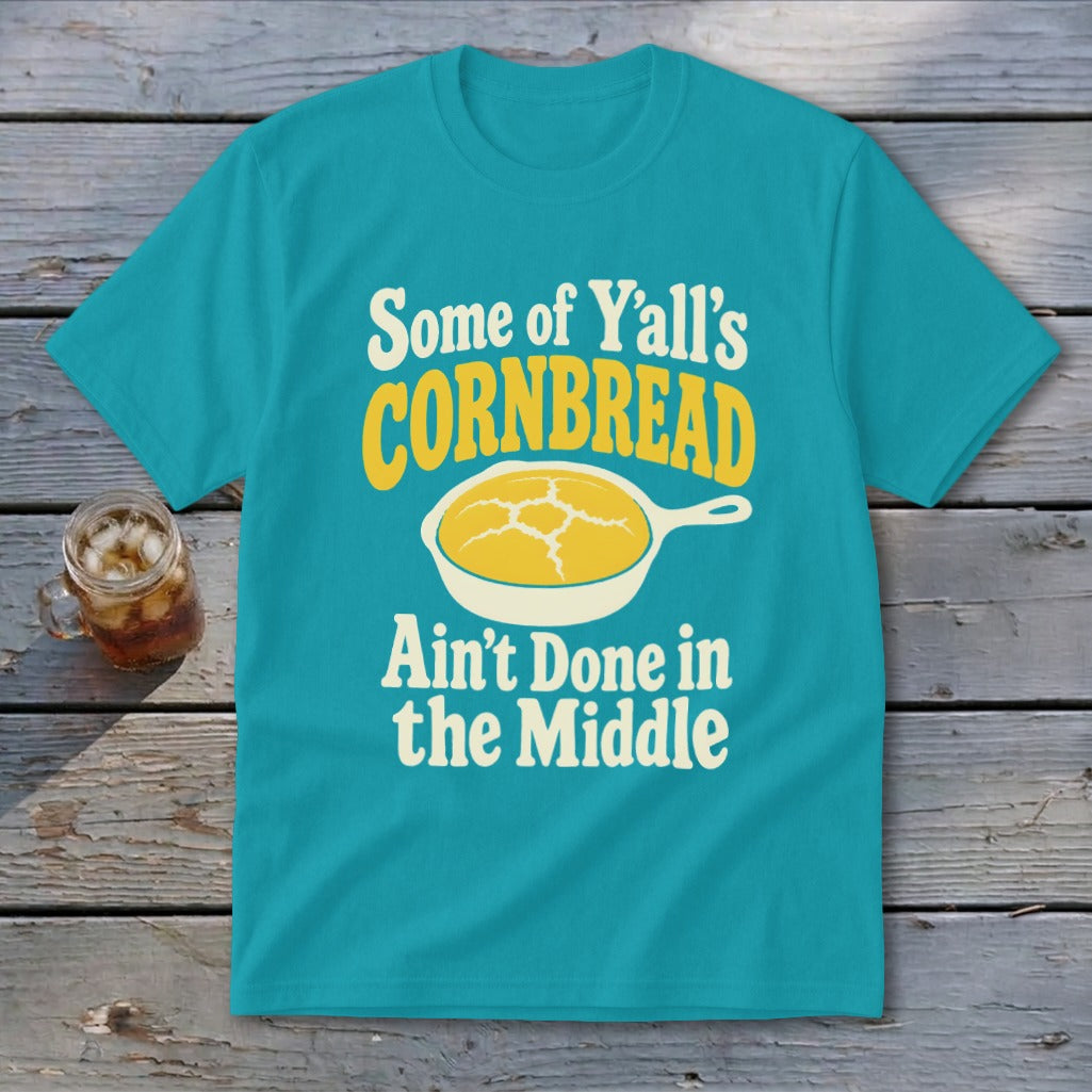 A turquoise t-shirt with the text "Some of Y'all's Cornbread Ain't Done in the Middle" and a skillet graphic.