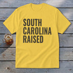 Yellow t-shirt with dark gray text reading "SOUTH CAROLINA RAISED."