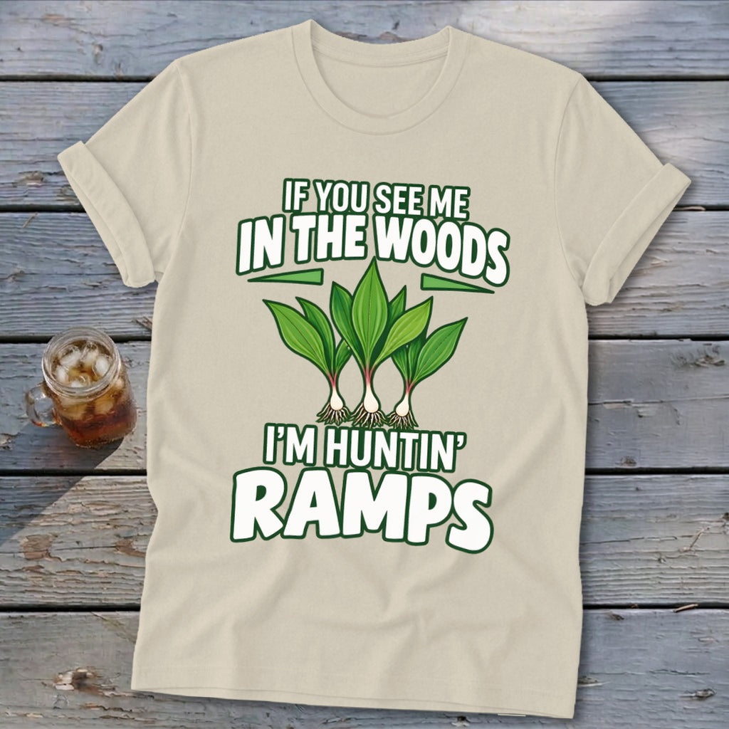 A cream-colored t-shirt displays green and white text that reads "IF YOU SEE ME IN THE WOODS I'M HUNTIN' RAMPS" above an illustration of ramp plants.