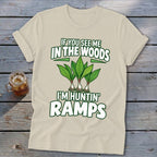 A cream-colored t-shirt displays green and white text that reads "IF YOU SEE ME IN THE WOODS I'M HUNTIN' RAMPS" above an illustration of ramp plants.