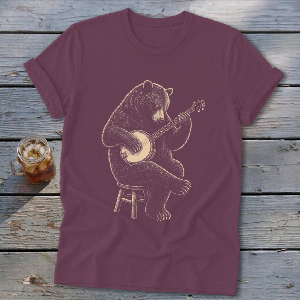 Brown bear sitting on stool playing a banjo on a maroon t-shirt.