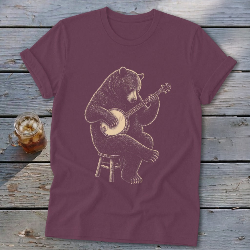 Brown bear sitting on stool playing a banjo on a maroon t-shirt.