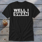 Black t-shirt featuring white text that reads WELL I SWAN laid flat on a rustic wooden surface.