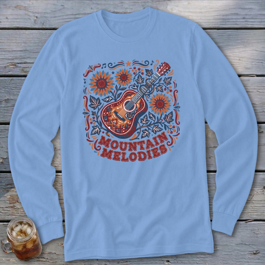 Light blue long-sleeve t-shirt with a folk-art graphic of an acoustic guitar, sunflowers, and the text MOUNTAIN MELODIES.