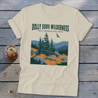 A cream-colored t-shirt featuring a stylized graphic of the Dolly Sods Wilderness with evergreen trees and mountains.
