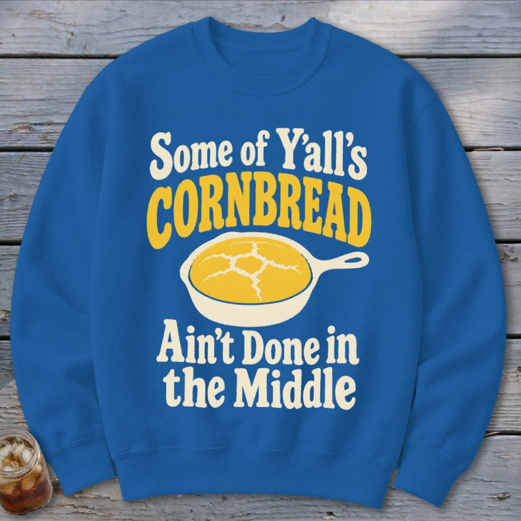 A blue crewneck sweatshirt featuring a graphic of cornbread in a skillet and text that reads Some of Y'all's Cornbread Ain't Done in the Middle.